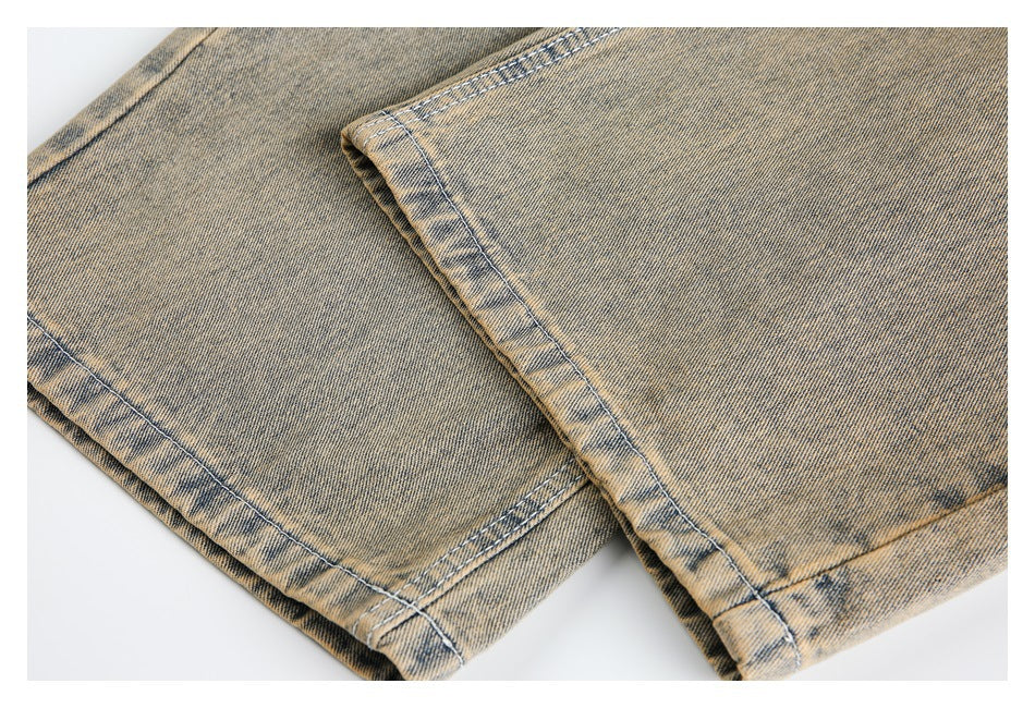 Close-up of the stitched leg hems on tan acid-wash jeans laid flat.