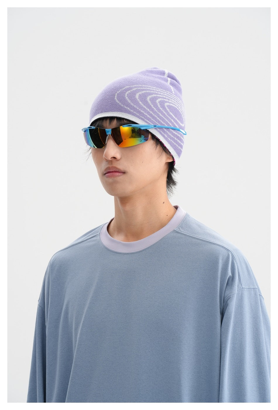 Close-up of a model in a light blue shirt with a lavender collar, patterned beanie, and mirrored sunglasses.