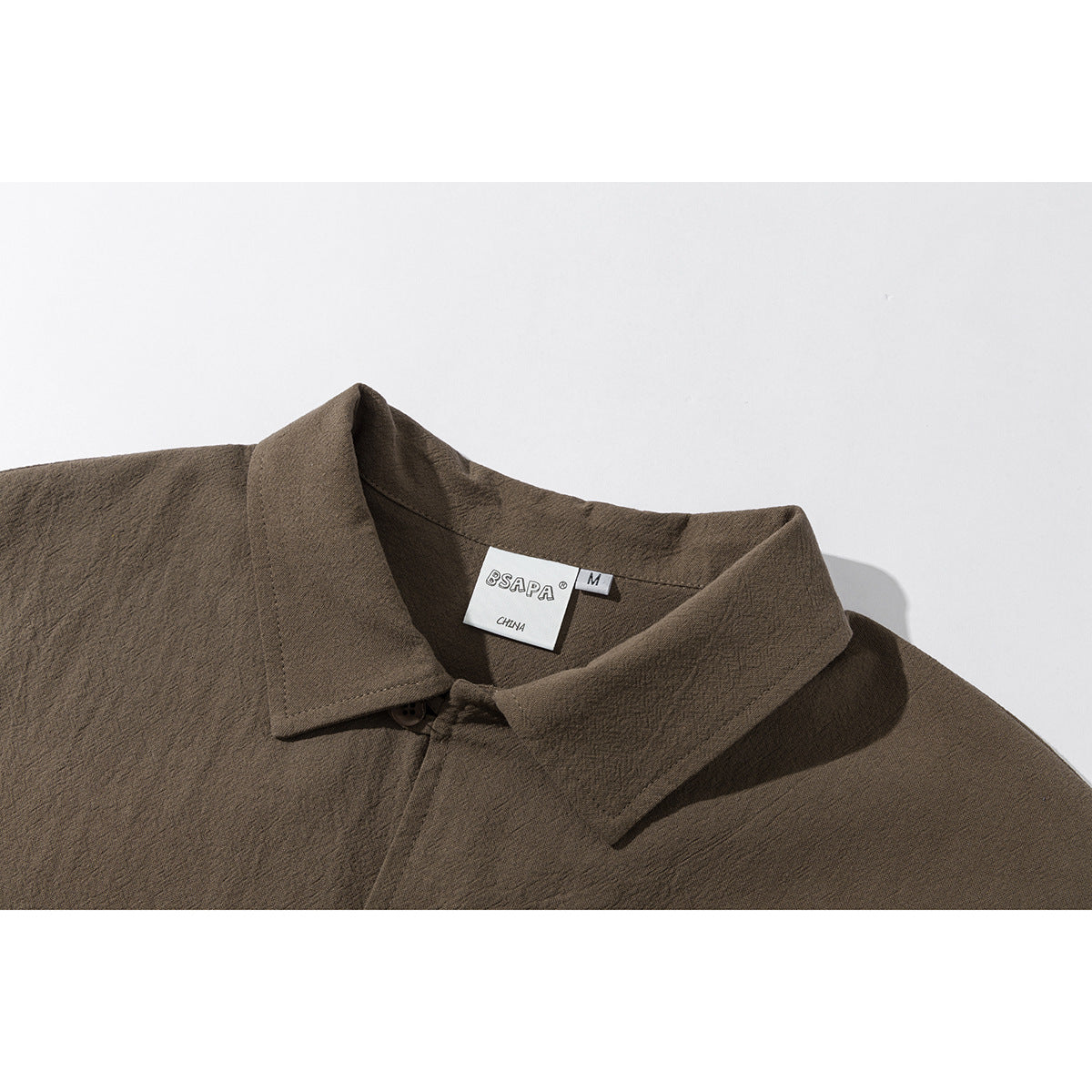 Close-up of a brown shirt's pointed collar, button, and neck label.