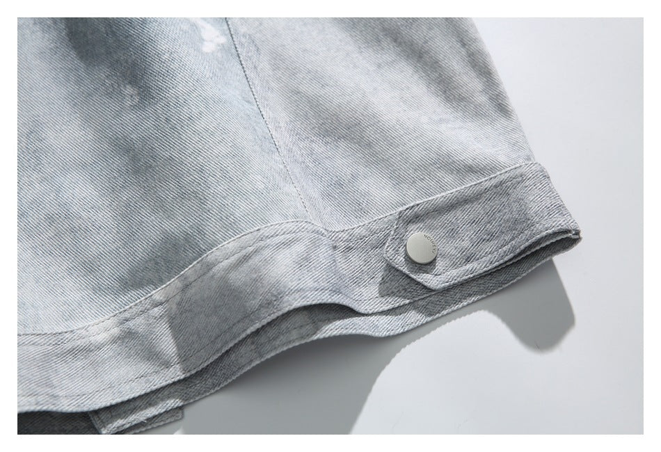 Close-up of a light gray denim garment hem with a stitched tab and round metal button.