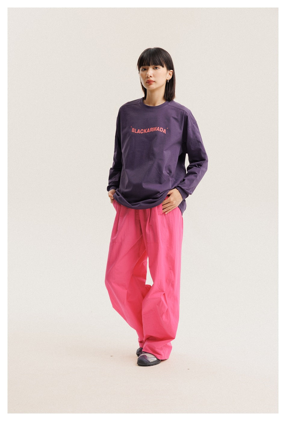 Model wearing a plum long-sleeve T-shirt with coral chest lettering and loose bright pink pants, front view.