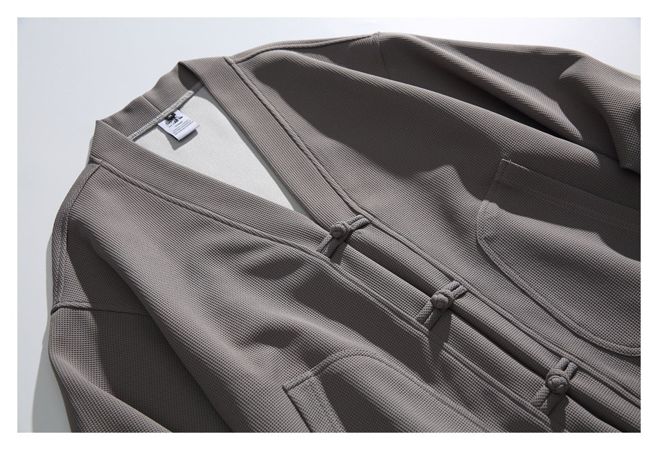 Close-up of a gray textured jacket with knotted frog closures, a patch pocket, and a small neck label.