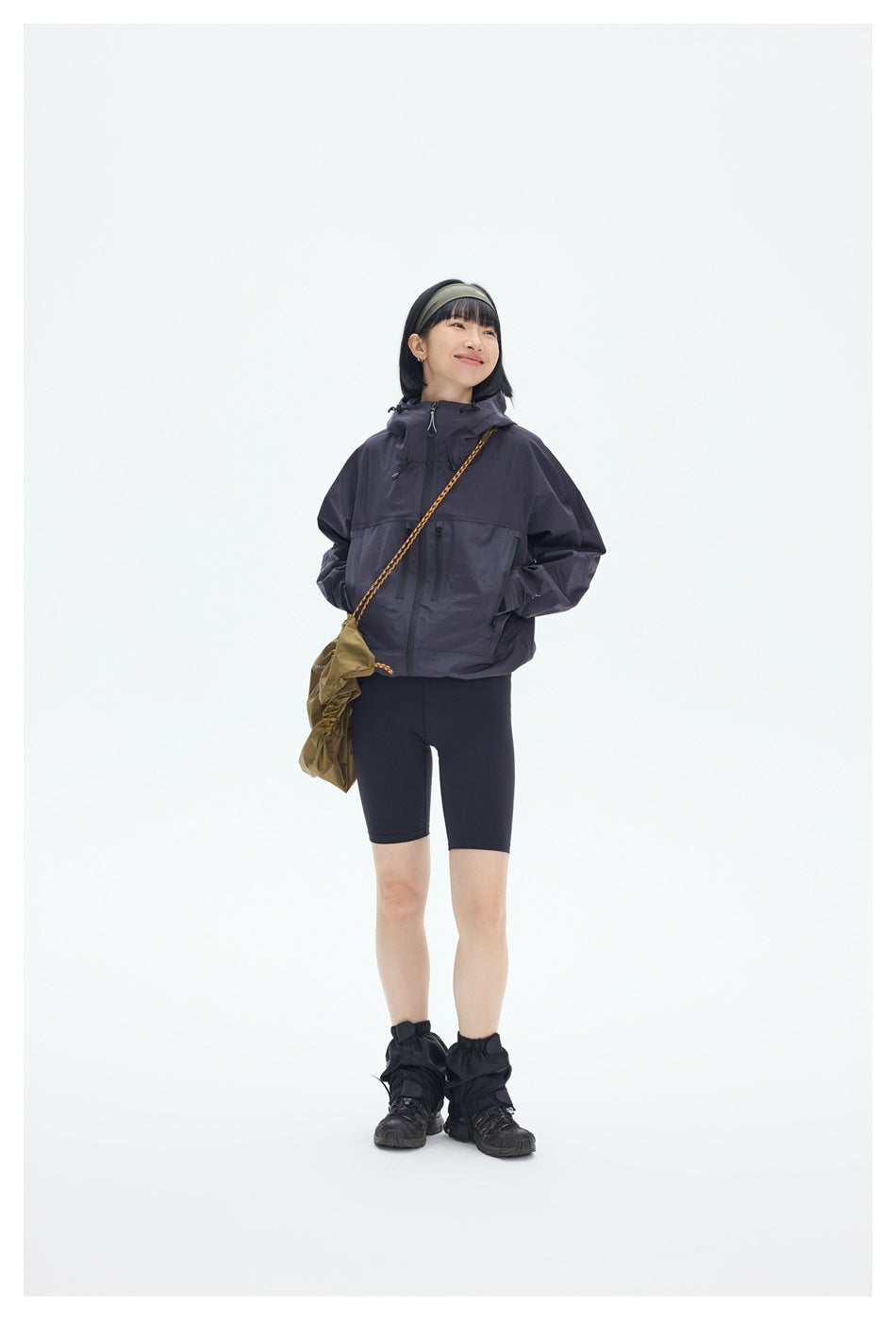 Model wears a dark plum hooded jacket with zip pockets, black cycling shorts and hiking gaiters.