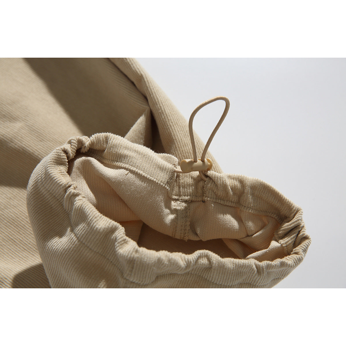 Close-up of a gathered beige pants cuff with an adjustable elastic drawcord and toggle.