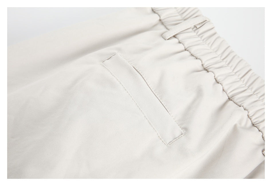 Close-up of a welt pocket and elastic waistband on light ivory trousers.