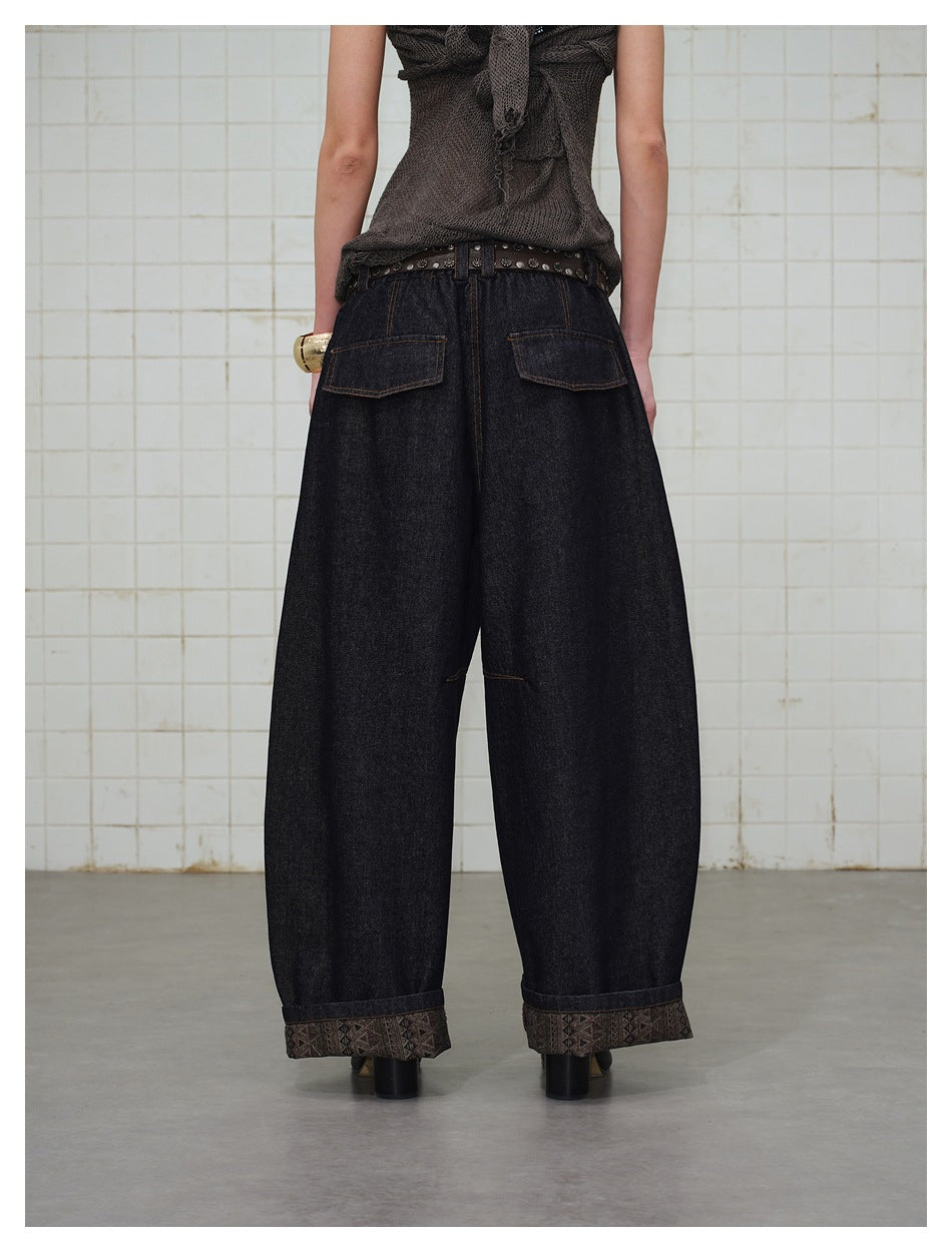 Back view of a person wearing dark wide-leg barrel jeans with flap back pockets and patterned cuffed hems