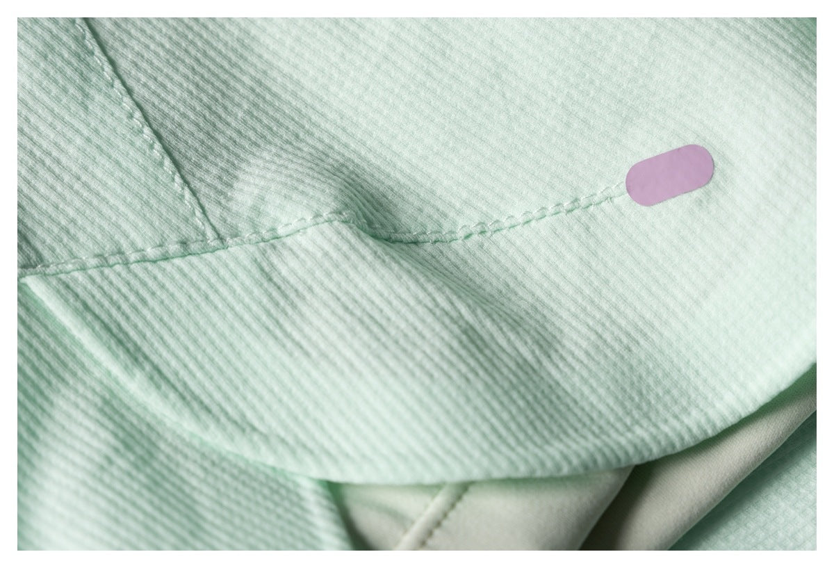 Close-up of pale mint textured fabric with a stitched seam and small blank lilac oval accent.