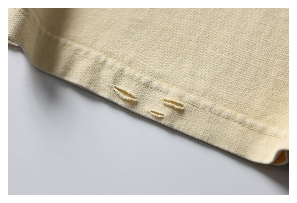 Close-up of small distressed holes beside the stitched hem of a pale cream T-shirt.