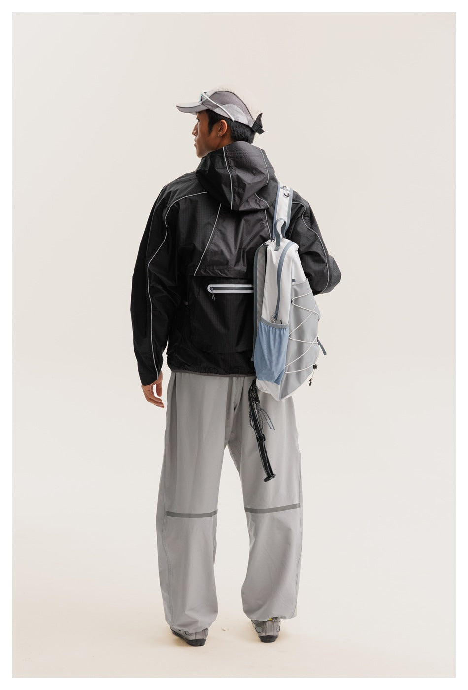 Back view of a model wearing a black hooded jacket and gray pants, with a light gray backpack.