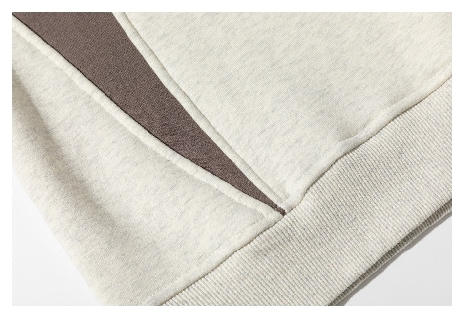 Close-up of an off-white sweatshirt hem with ribbed trim and a dark brown panel.
