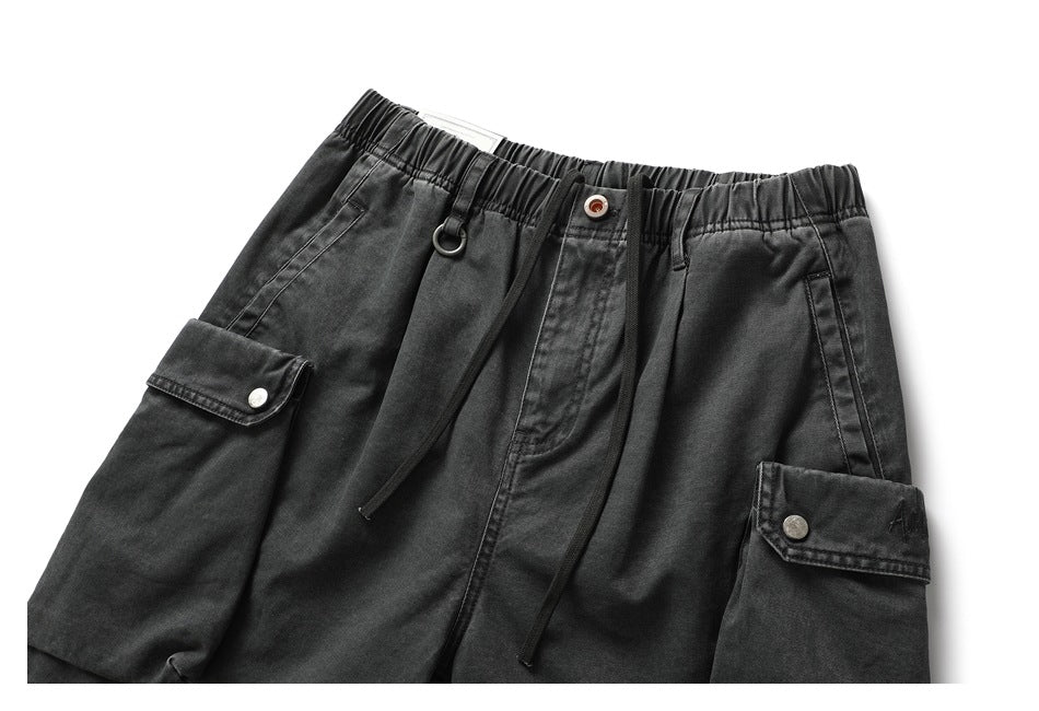 Cropped front view of charcoal cargo shorts with an elastic waist, drawstring, front pockets, and snap-button cargo pockets.