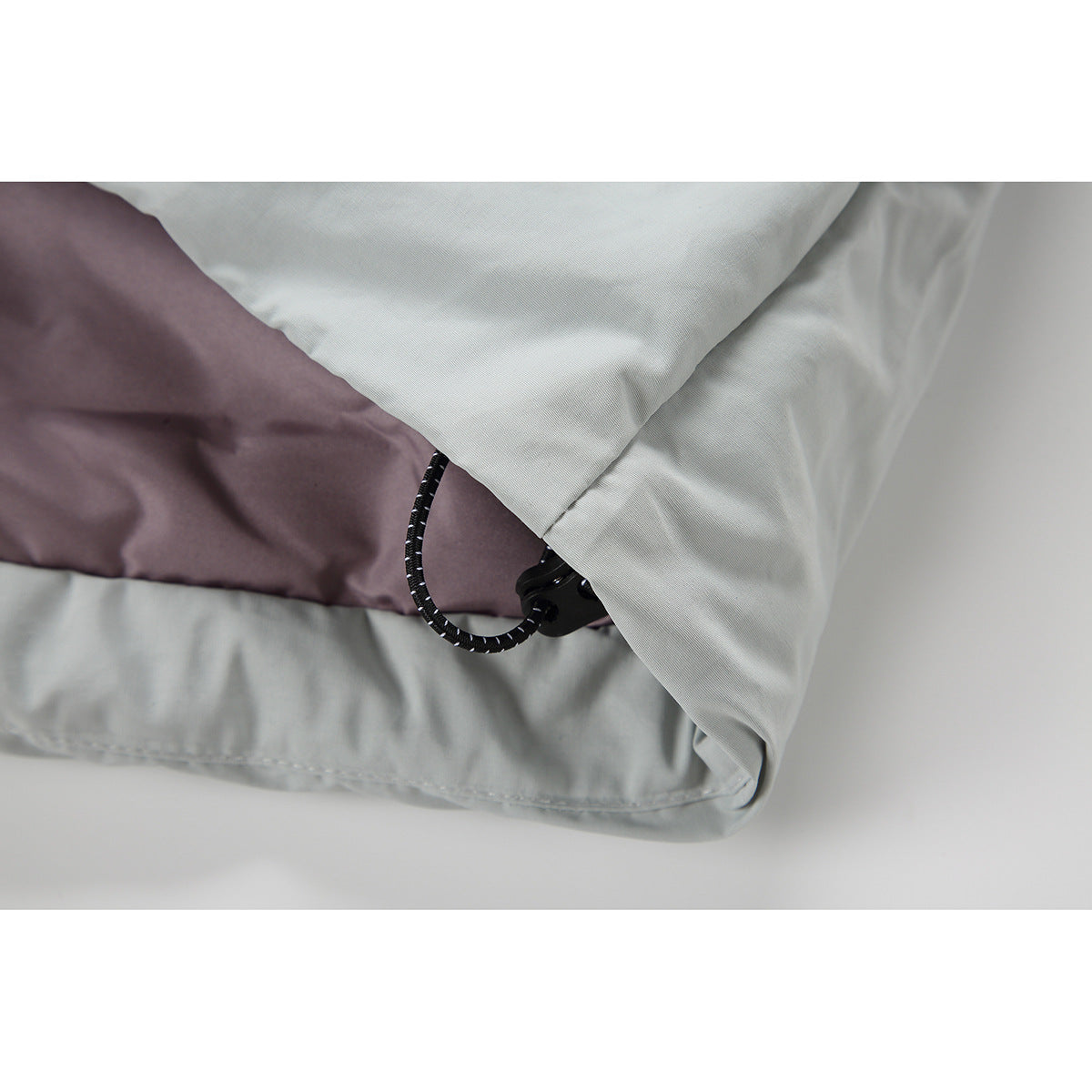 Close-up of a pale gray jacket hem with a black elastic drawcord and toggle beside mauve lining.