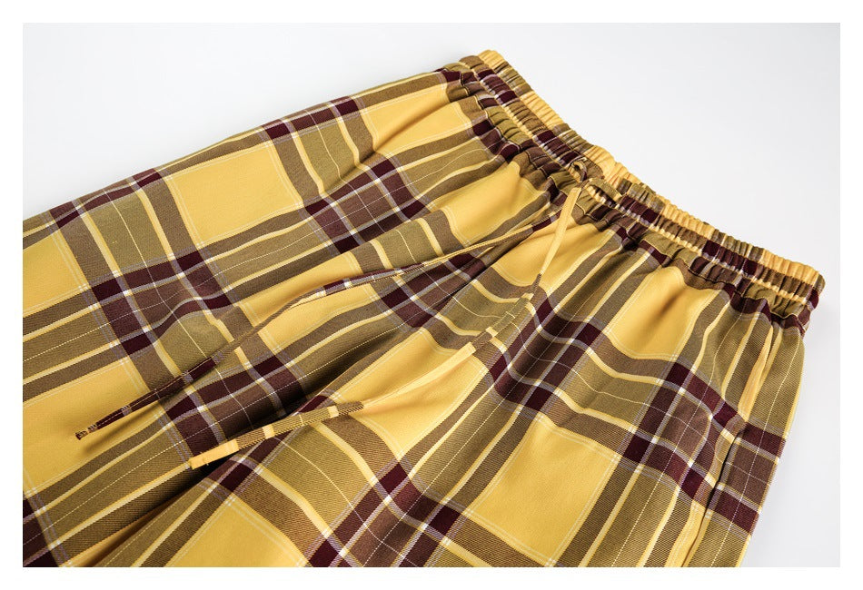 Close-up of mustard yellow plaid pants with an elastic waistband and matching drawstrings, laid flat.