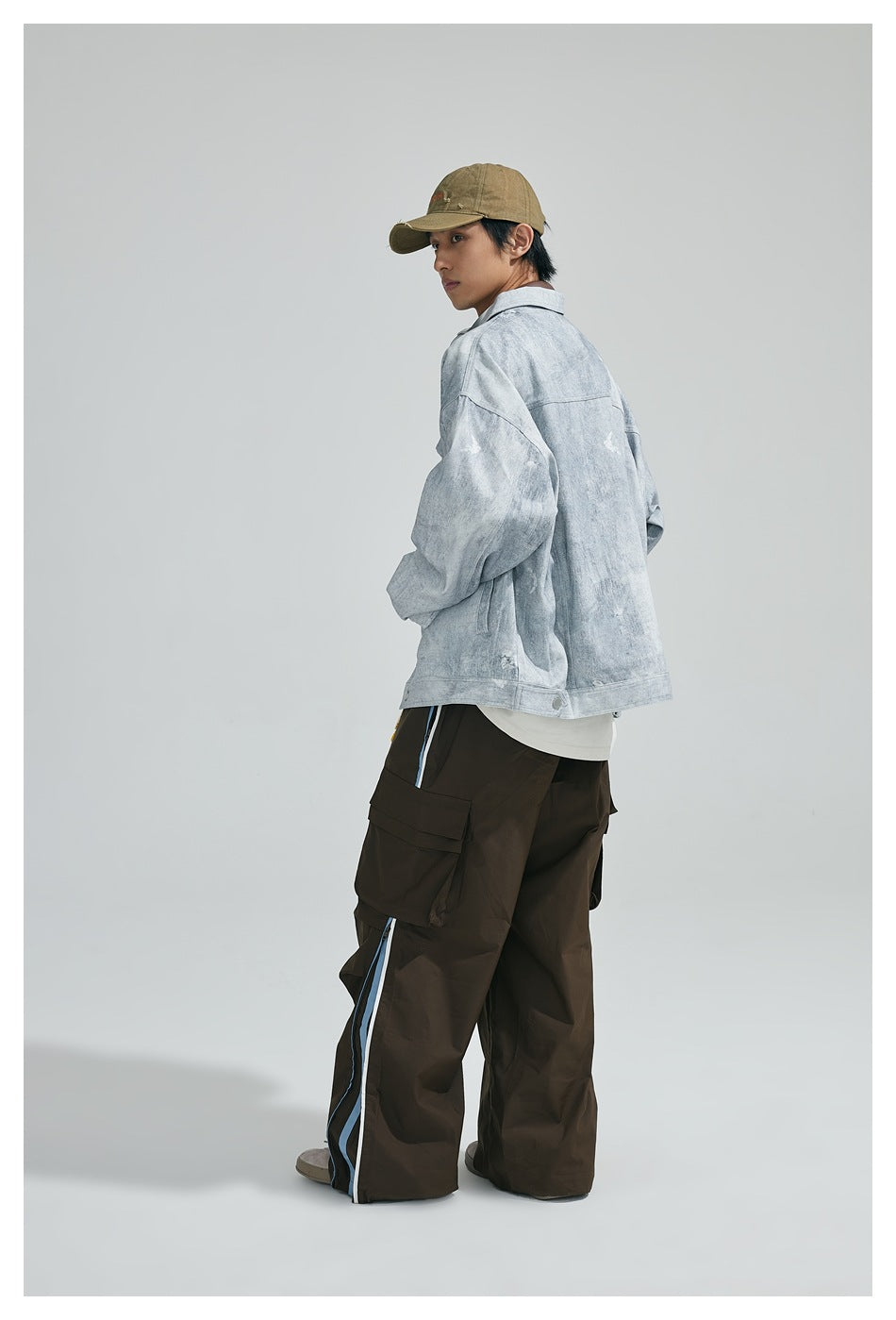 Rear three-quarter view of a model wearing a light gray washed jacket and dark cargo pants with blue side stripes.