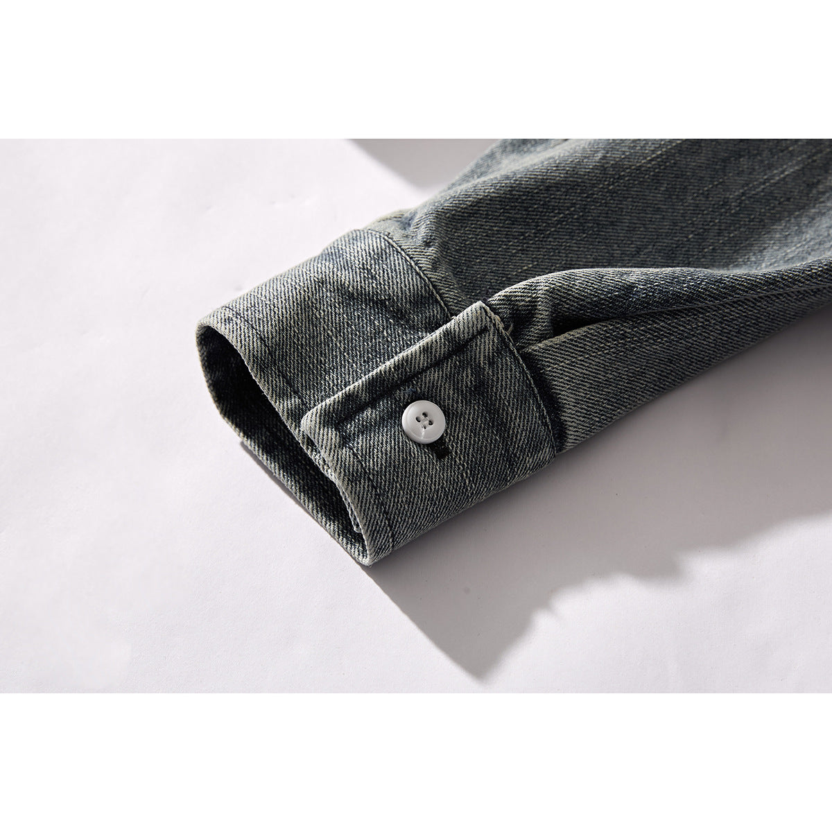 Close-up of a dark gray washed denim shirt cuff with a single white button.