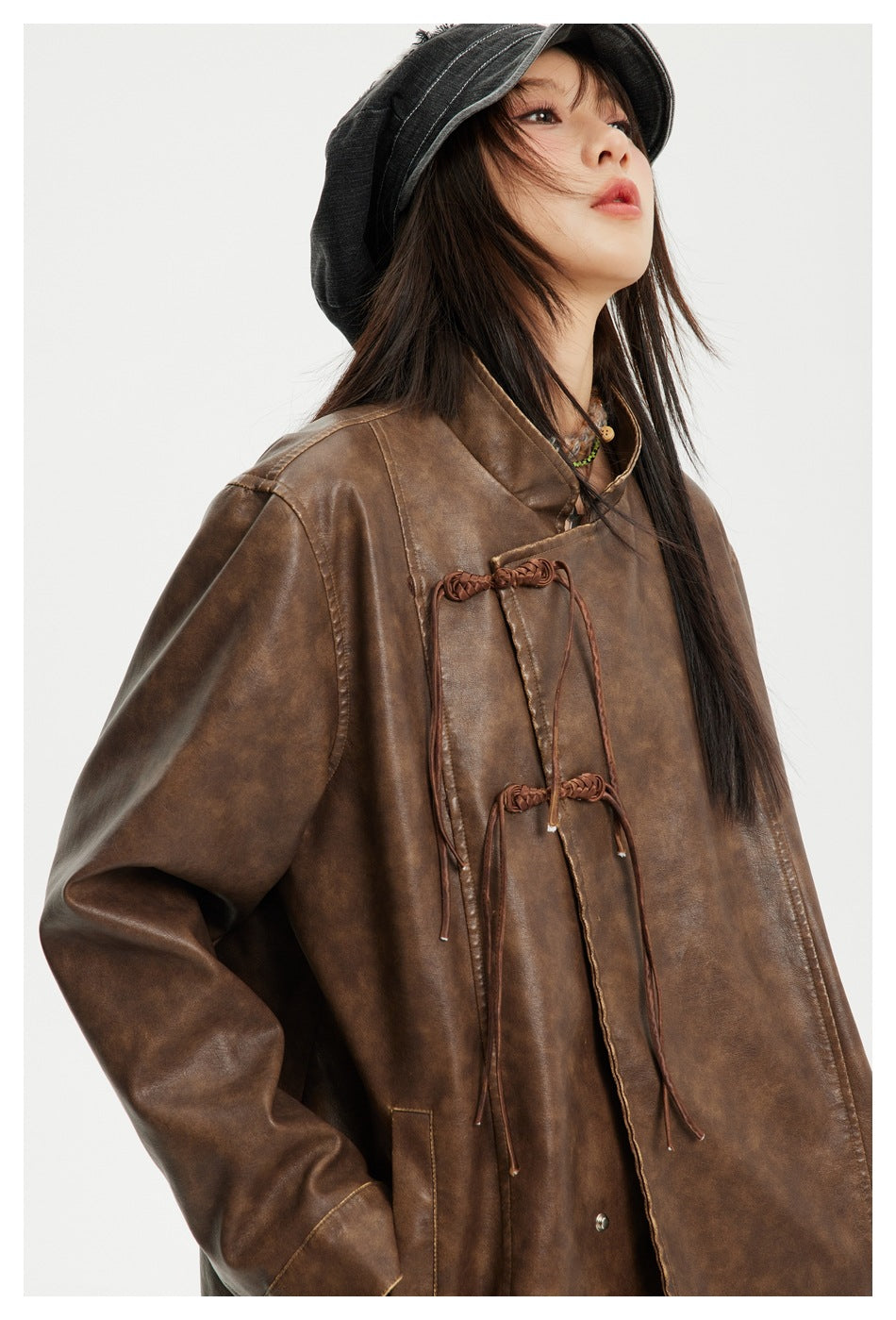 Close view of a model wearing a brown jacket with a high collar and braided tie closures.