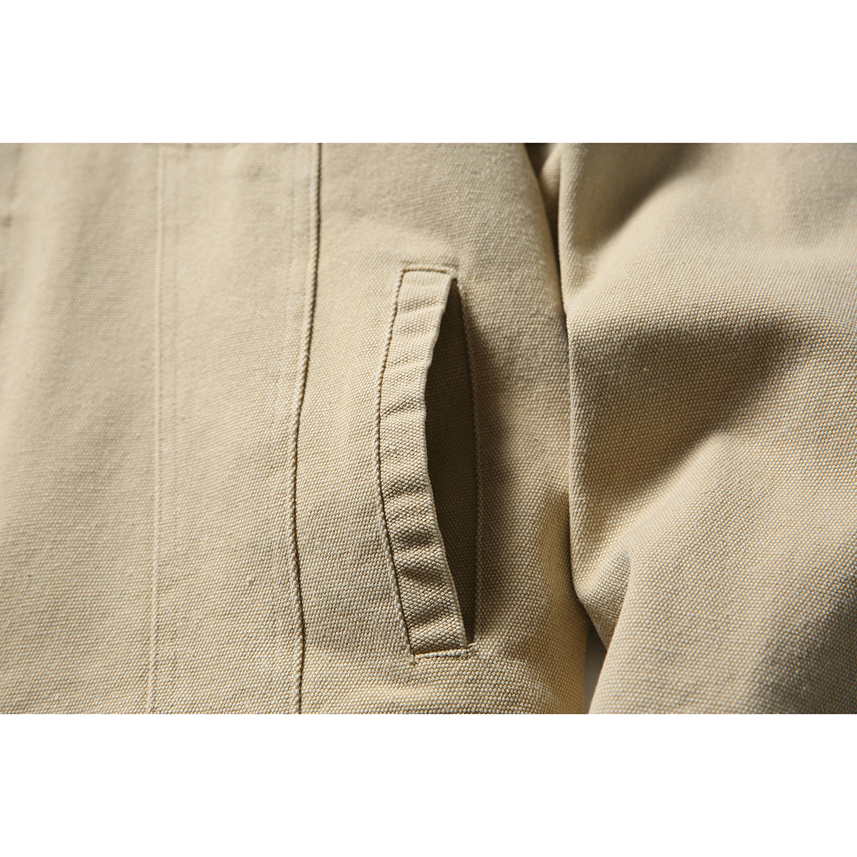 Close-up of a sand-colored jacket’s angled welt pocket and textured fabric.