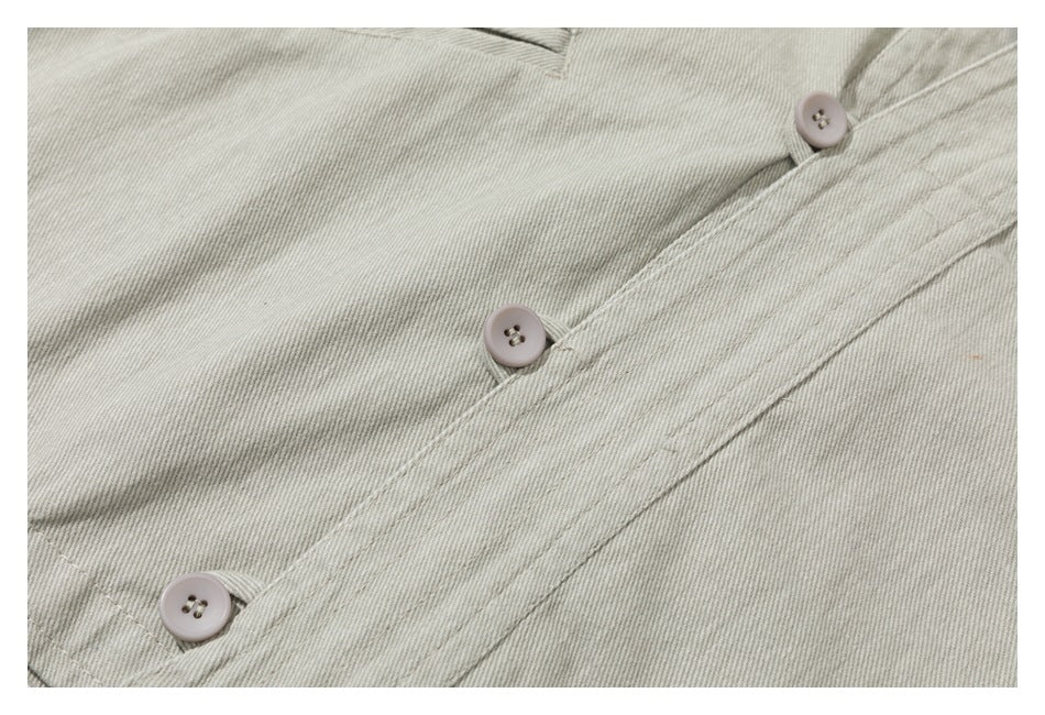 Close-up of a pale gray-beige garment with a diagonal button placket, three light buttons, and visible stitching.