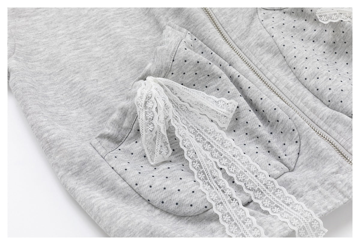 Close-up of a gray garment showing a dotted pocket with white lace trim and a metal zipper.