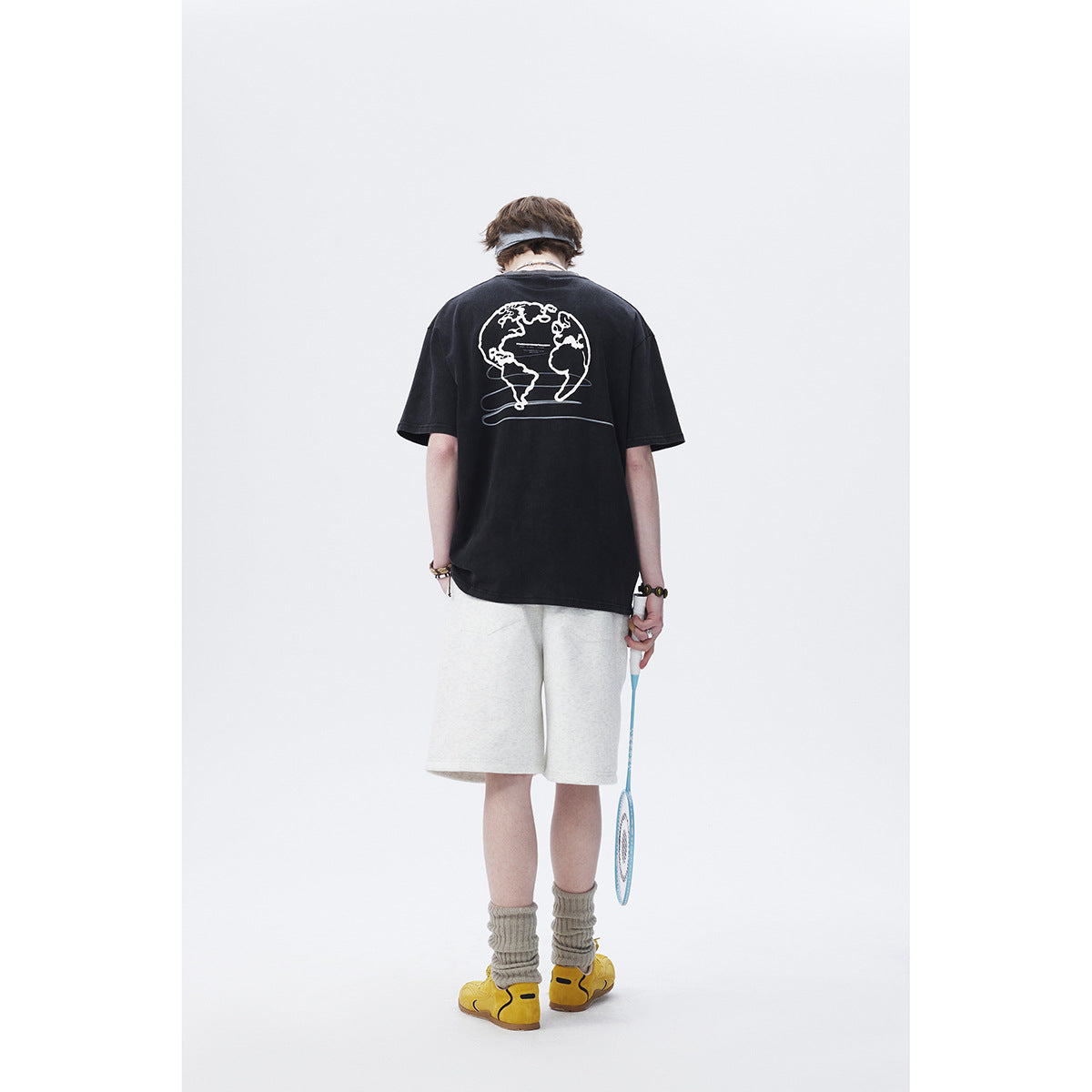 Rear view of a model wearing a black oversized T-shirt with a white globe graphic and light shorts.