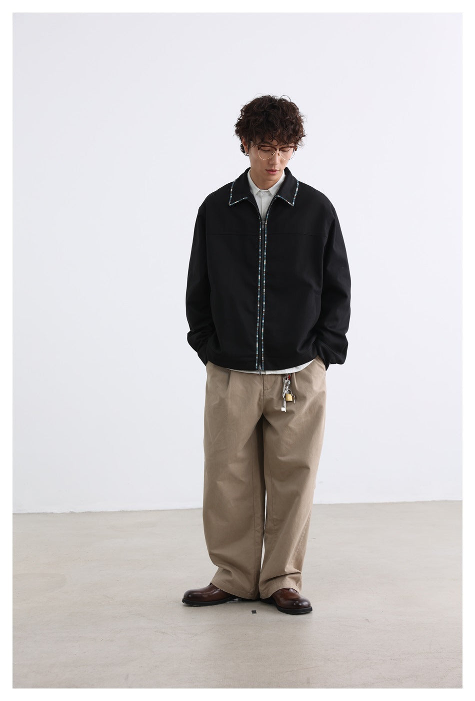 Full-length front view of a model wearing a black jacket with multicolor trim and loose tan trousers.