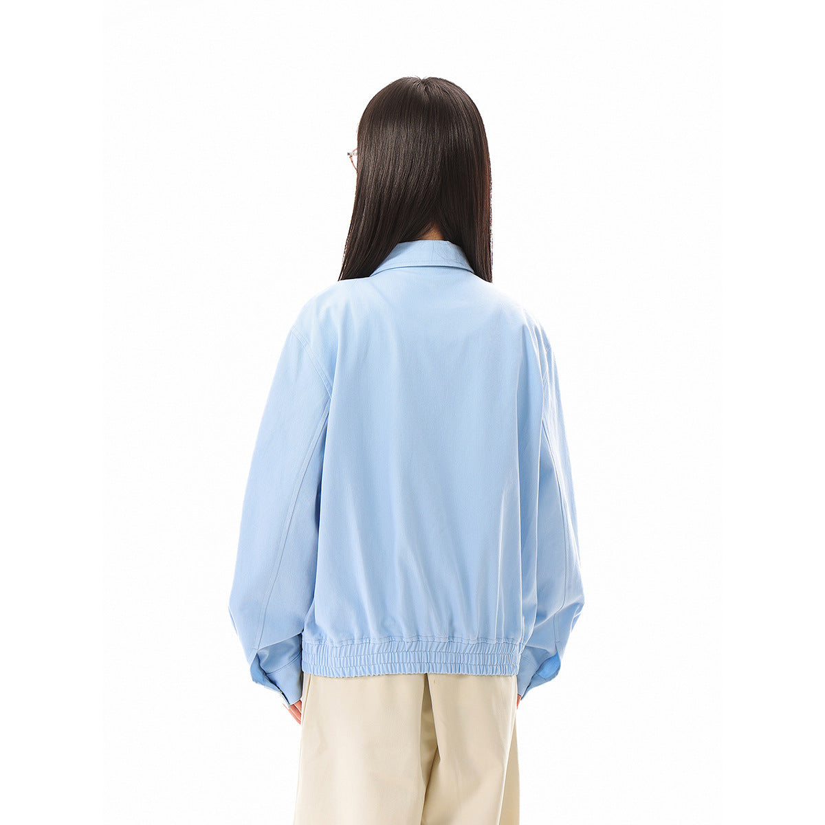 Back view of a model wearing a light blue jacket with a plain back, long sleeves, and a gathered elastic hem.