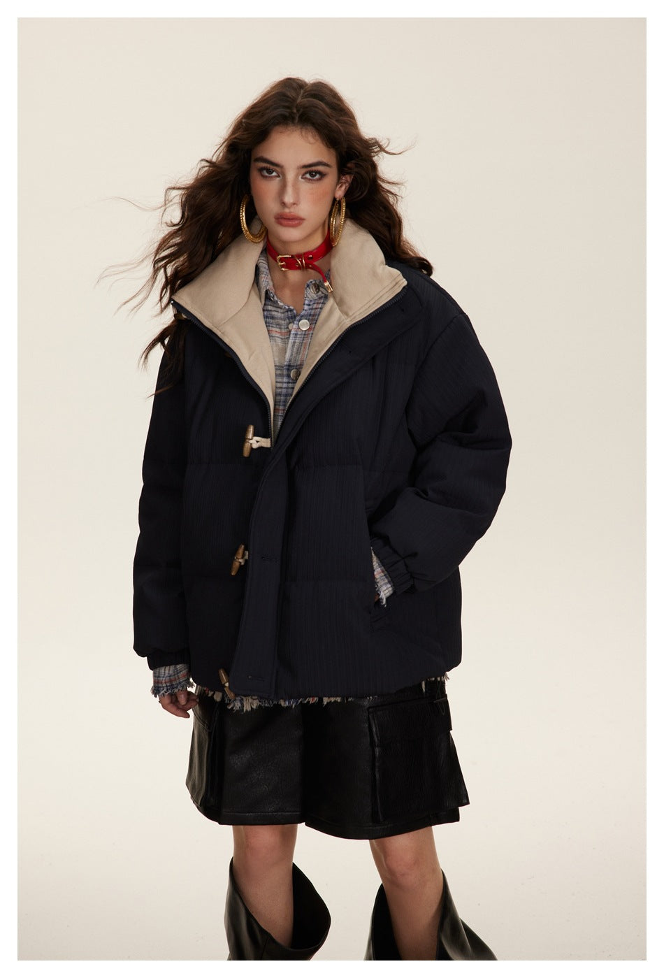 Close-up of model wearing a navy puffer jacket with toggle closures and a beige inner collar over a plaid shirt