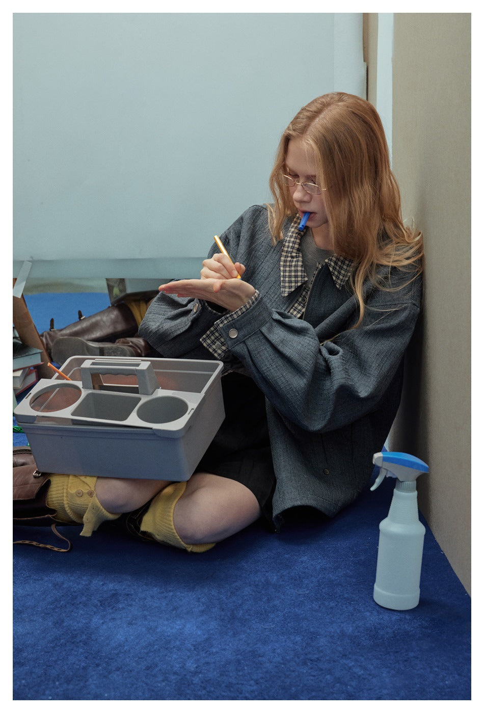 Seated model wearing an oversized charcoal jacket with checked collar and cuffs over a gray top.