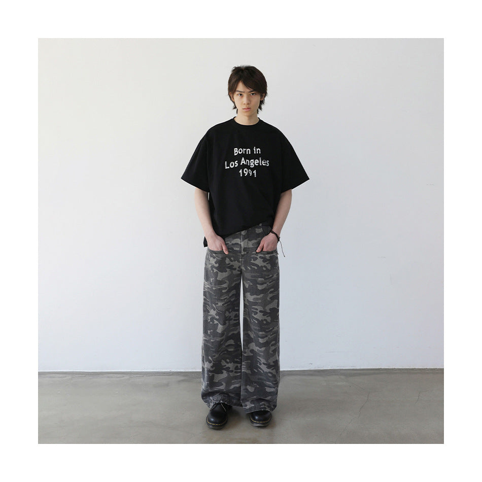 Model wearing a black graphic T-shirt with wide gray camouflage trousers, shown full length.