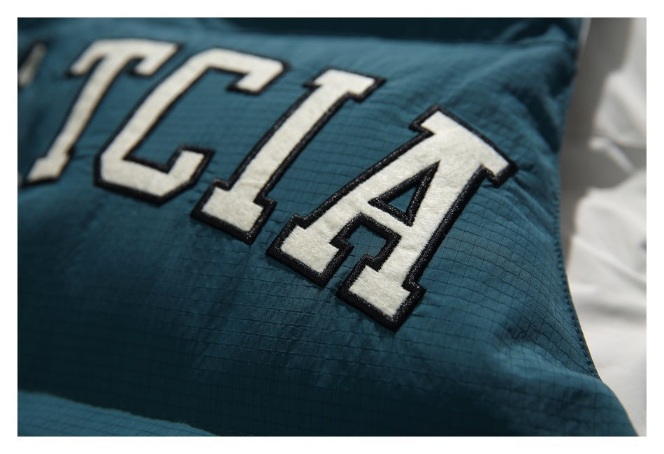 Close-up of raised cream varsity-style lettering with black edging on the dark teal vest.