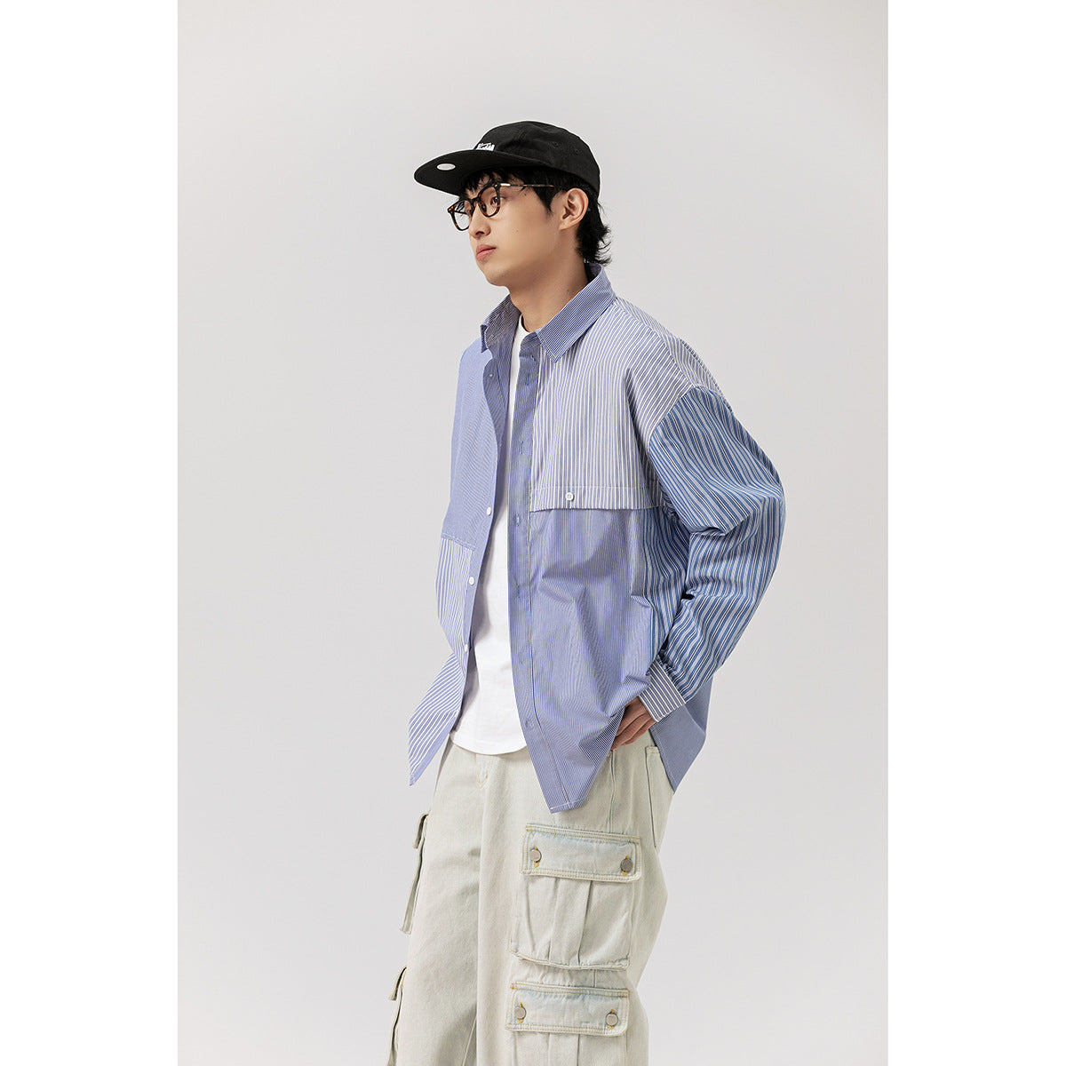 Model wearing a blue patchwork striped button-up shirt over a white tee, with pale cargo pants.