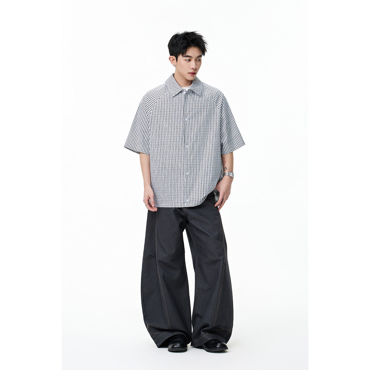 Model wearing a gray-and-white gingham short-sleeve button-up shirt with dark wide-leg trousers.