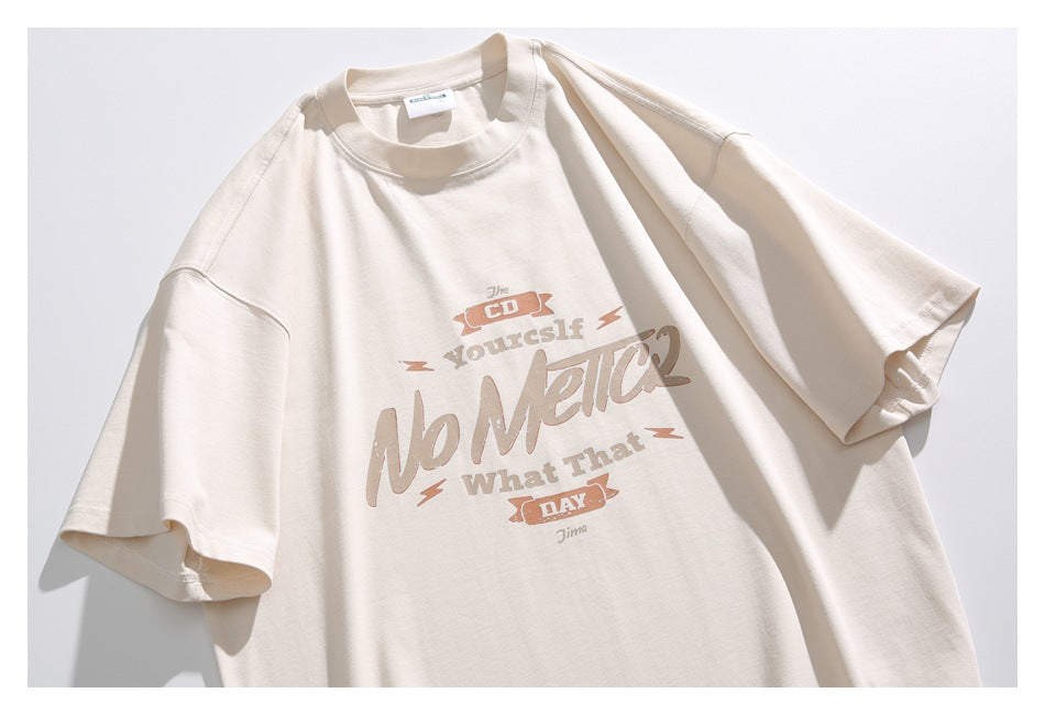 Flat-lay front view of a cream short-sleeve T-shirt with a large brown and tan English text graphic.