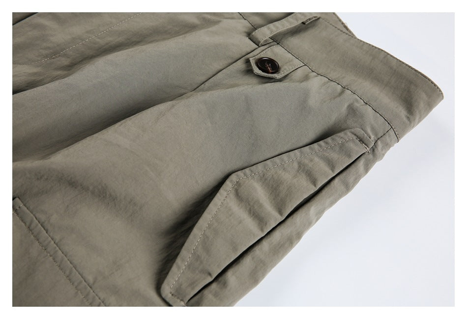 Close-up of olive-gray trousers showing a dark button and a stitched flap pocket.