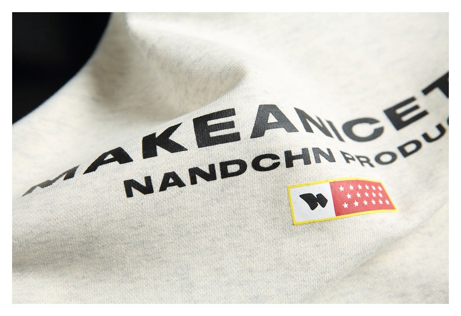 Close-up of black lettering and a small red-and-yellow graphic printed on the off-white sweatshirt chest.