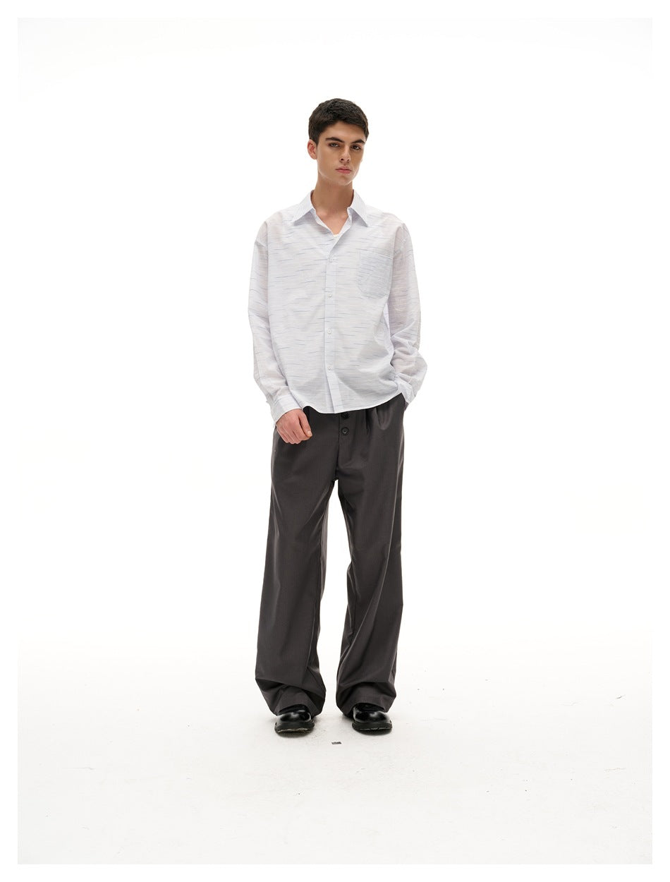 Model standing facing forward in a light striped long-sleeve shirt with chest pocket, wearing gray wide-leg trousers