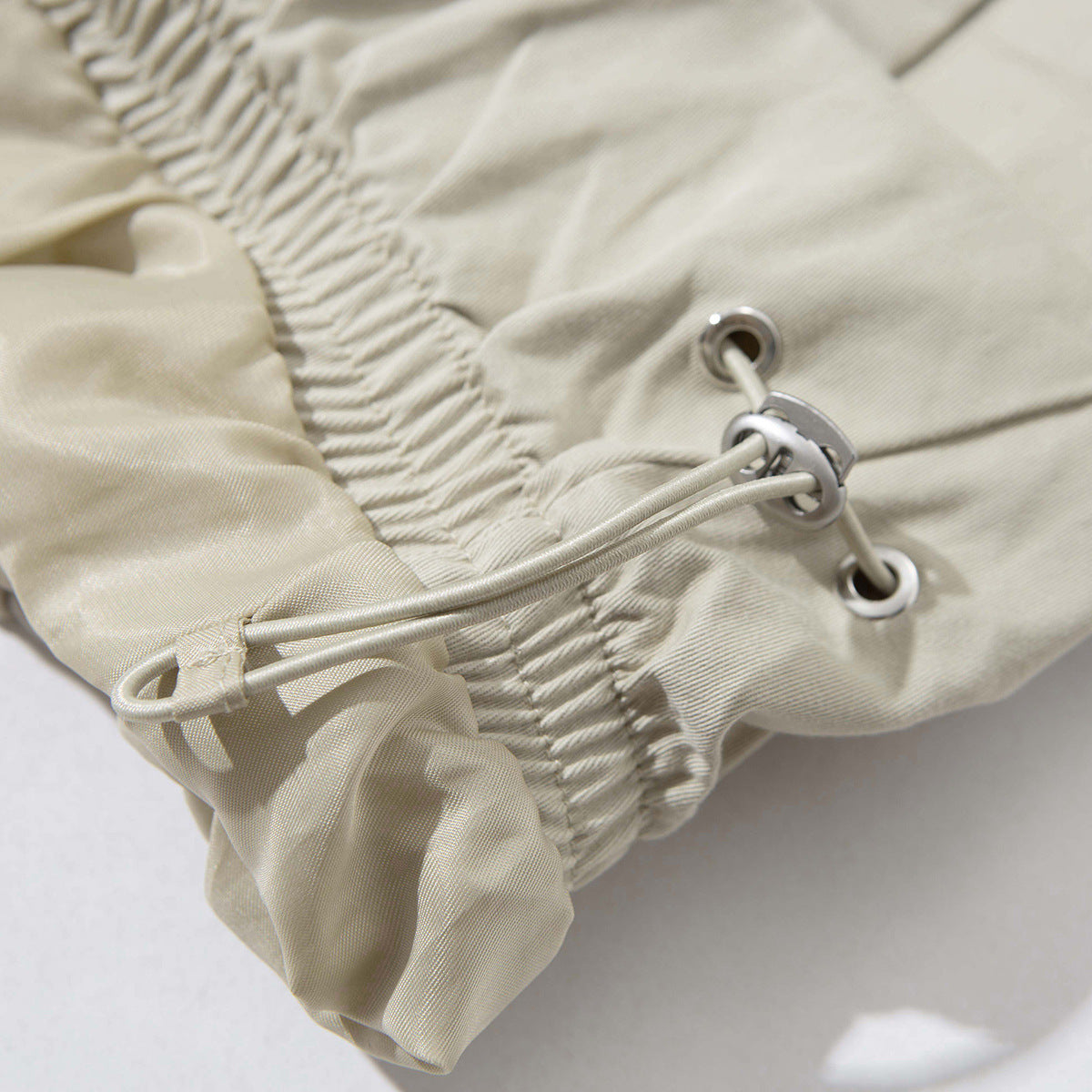 Close-up of the light beige jacket's gathered hem and adjustable drawcord with metal eyelets.