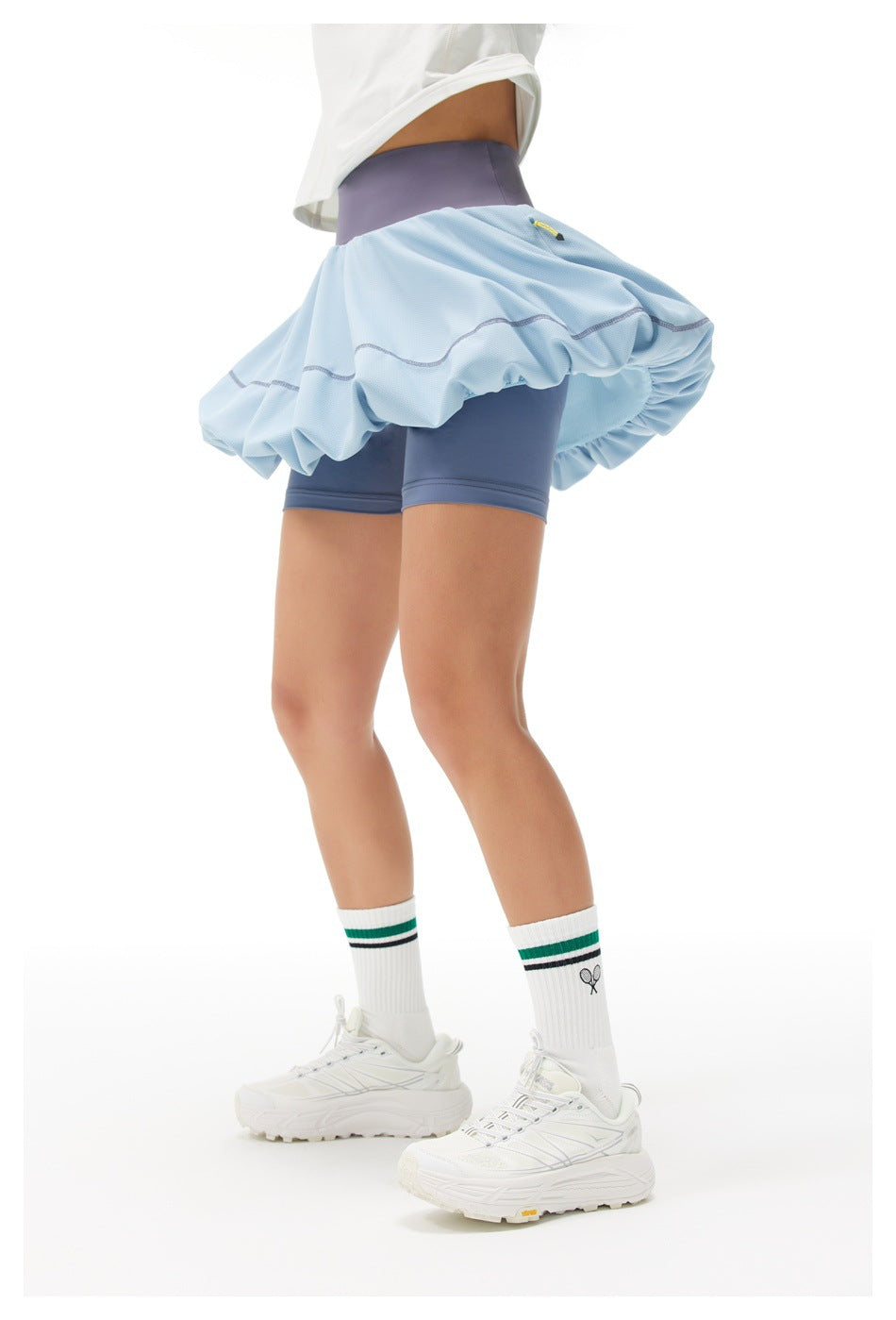Side view of a model wearing a light blue bubble tennis skirt with a dark blue waistband and matching built-in shorts.