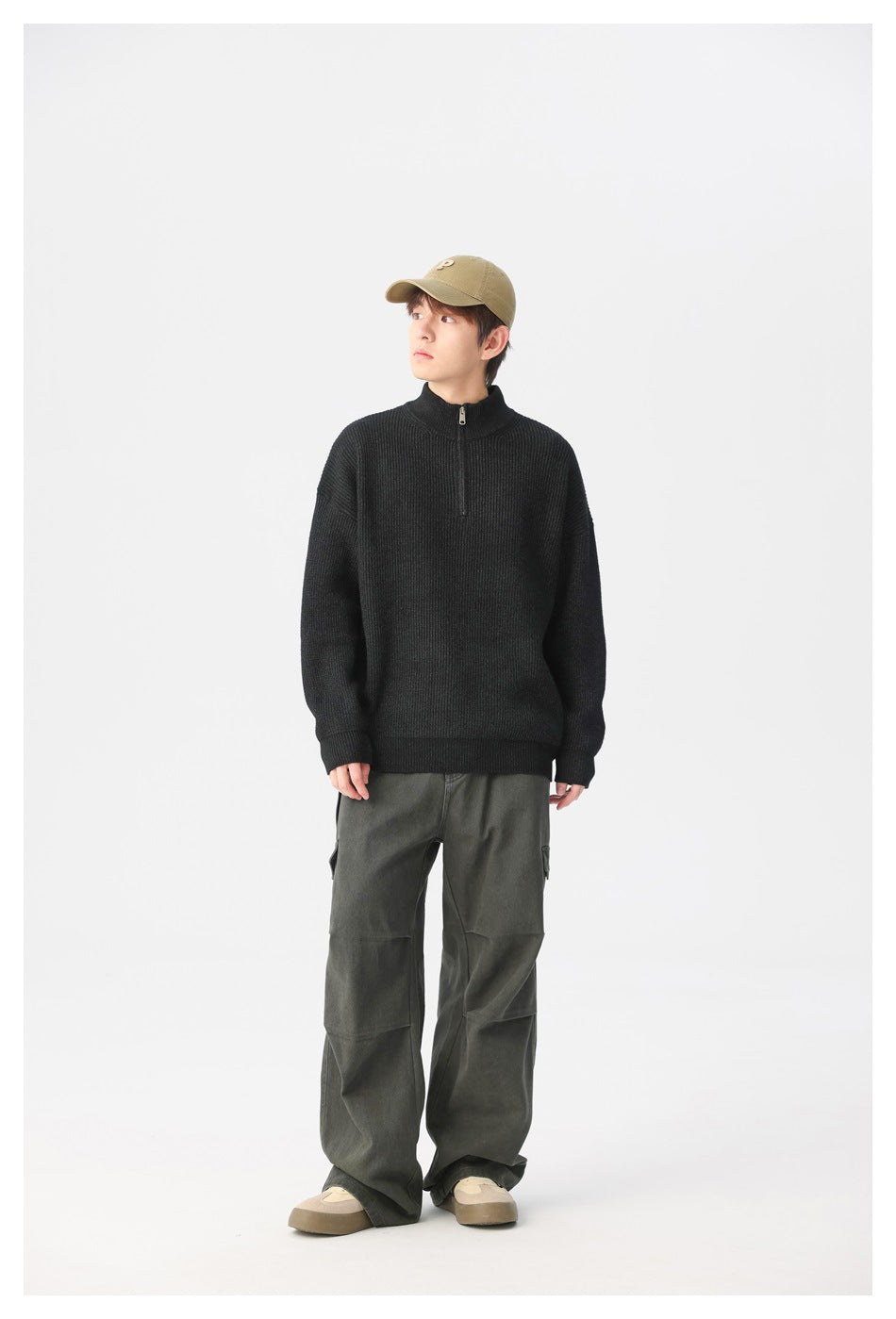 Front view of a model wearing a black ribbed quarter-zip sweater with loose dark gray trousers.