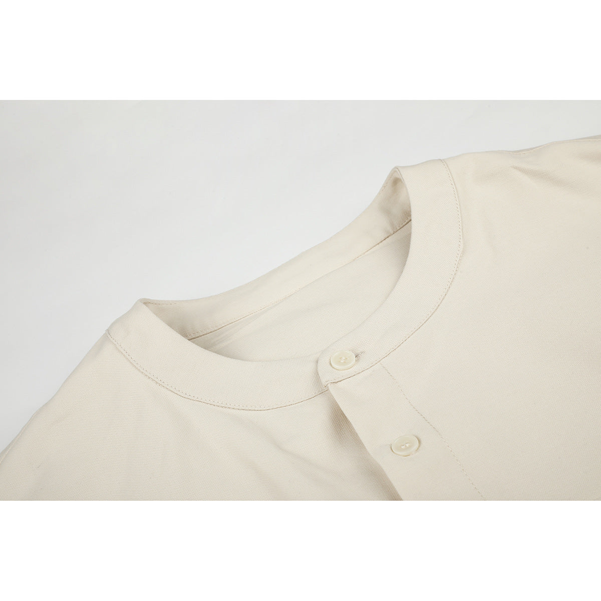 Close-up of an ivory shirt's band collar, button fastening, and neat stitching.