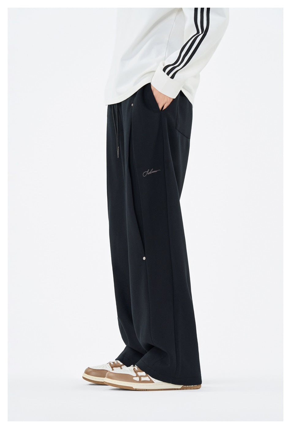 Side view of a model wearing loose black wide-leg trousers with a snap-button panel and small script detail.