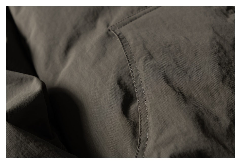 Close-up of a curved stitched seam and gathered fabric on a dark olive jacket.