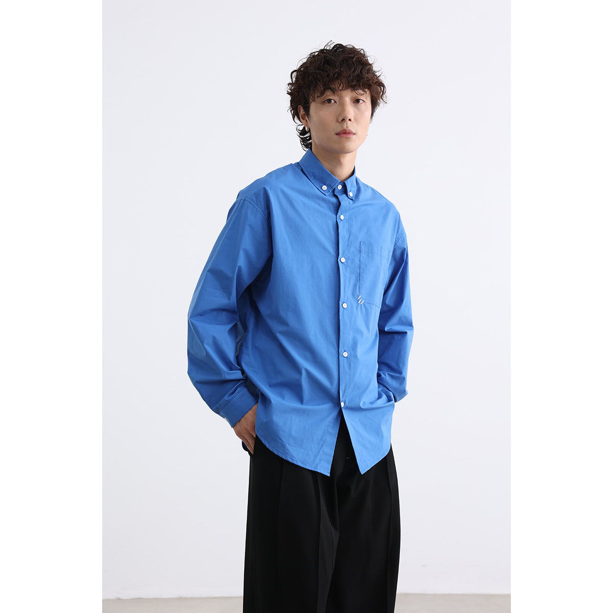 Model wearing a bright blue button-down shirt with a chest pocket and black trousers.