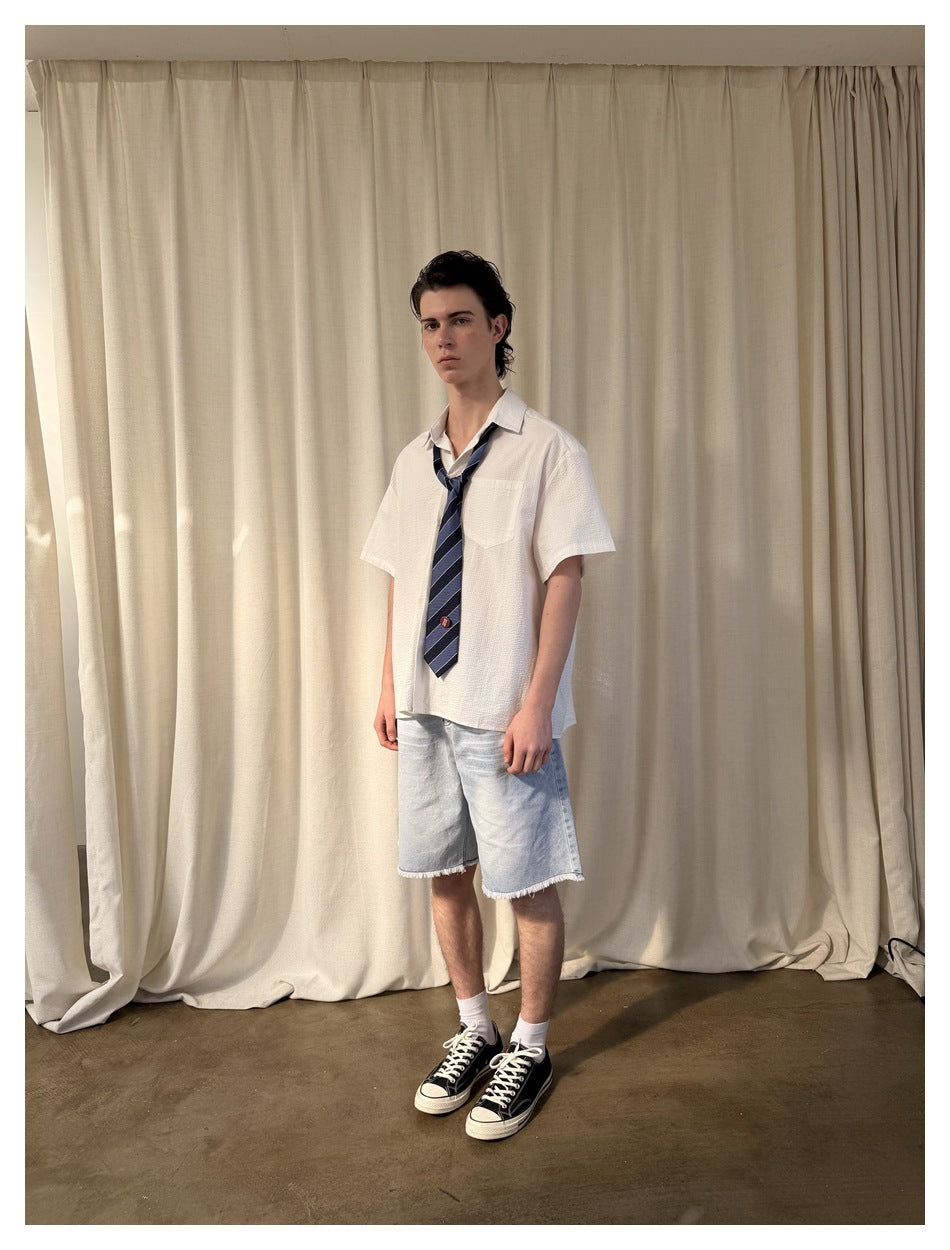 Three-quarter front view of a model in a white short-sleeve shirt with chest pocket and striped navy tie.