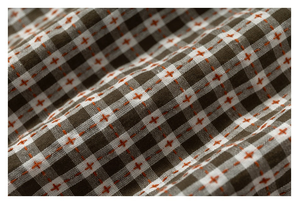 Macro view of brown, gray, and cream checked fabric with orange cross-stitch details and a woven texture.