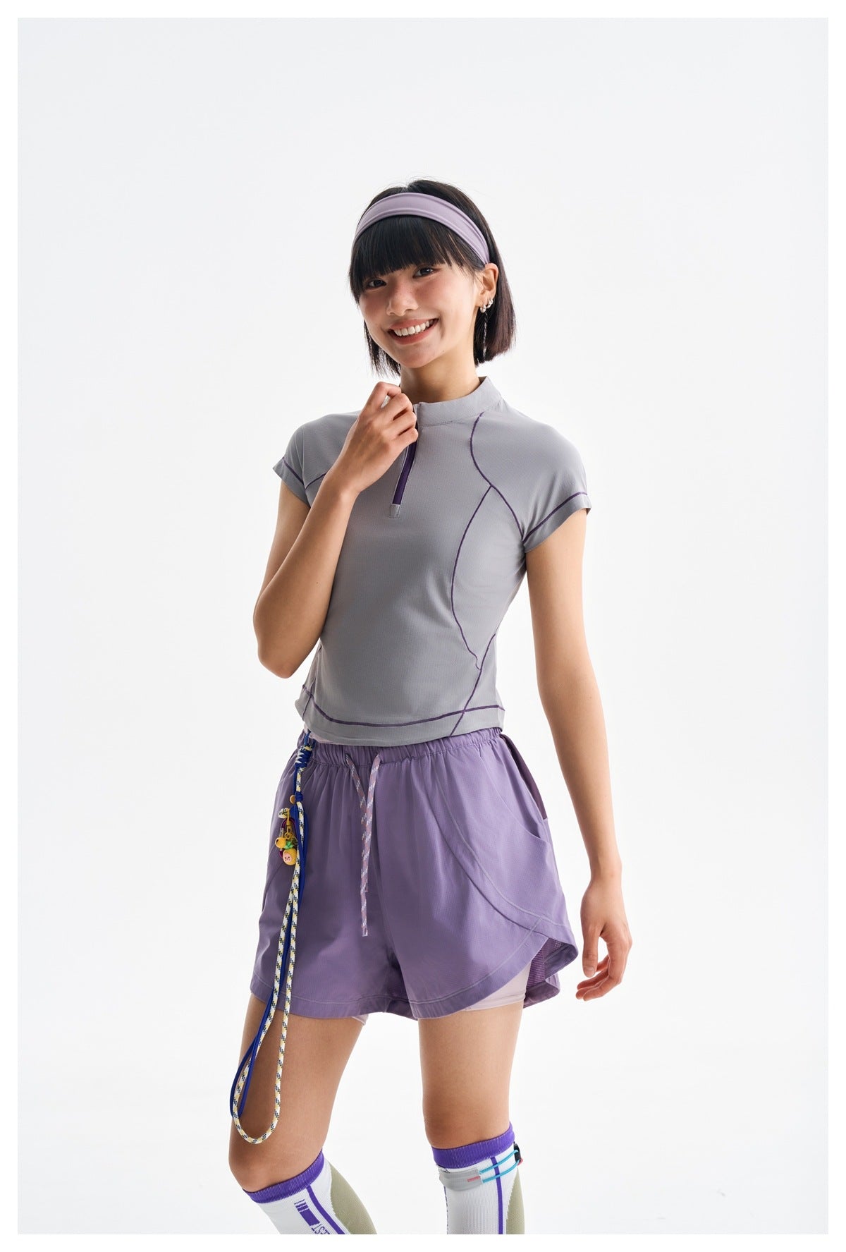 Closer view of a model wearing a gray-lavender zip-neck top and purple shorts with layered hems.