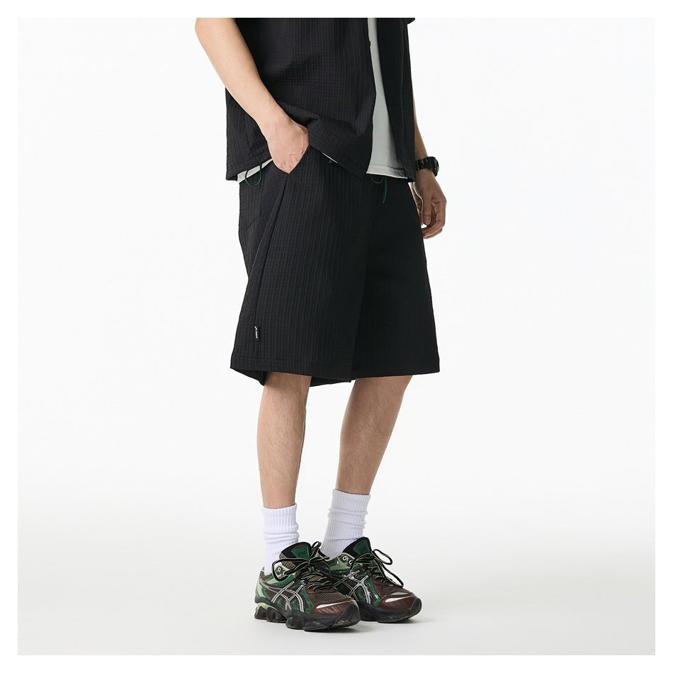 Model wearing black textured wide-leg shorts with a matching top, white socks and sneakers, side view, hand in pocket
