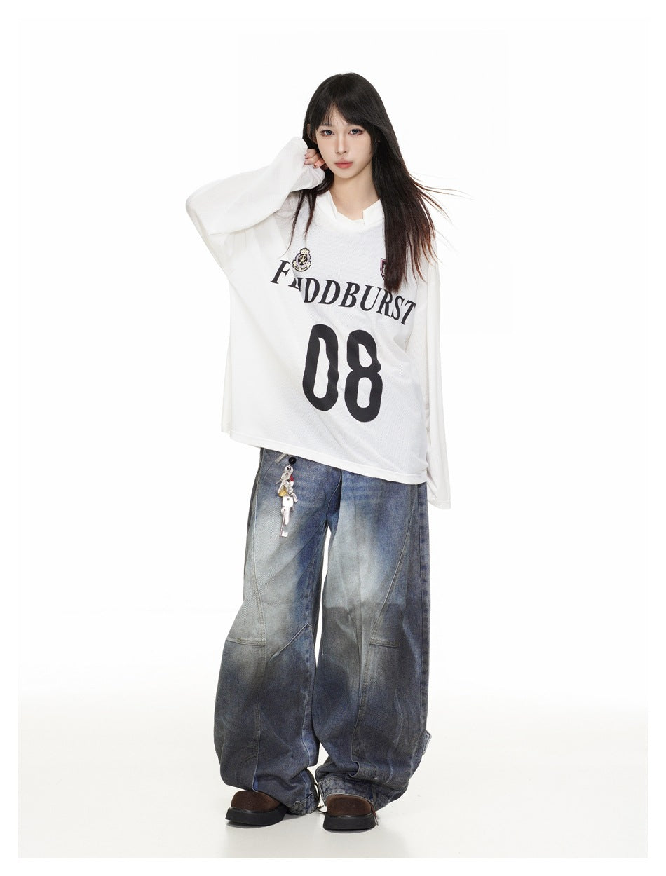 Model in the white oversized jersey-style top with long sleeves, 08 print and faded wide-leg jeans, hand raised to hair
