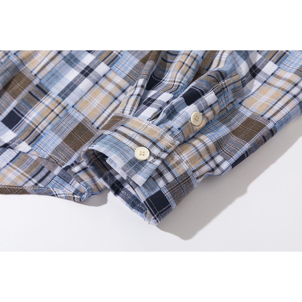 Close-up of the buttoned cuff on a blue, brown, navy, and white plaid shirt.