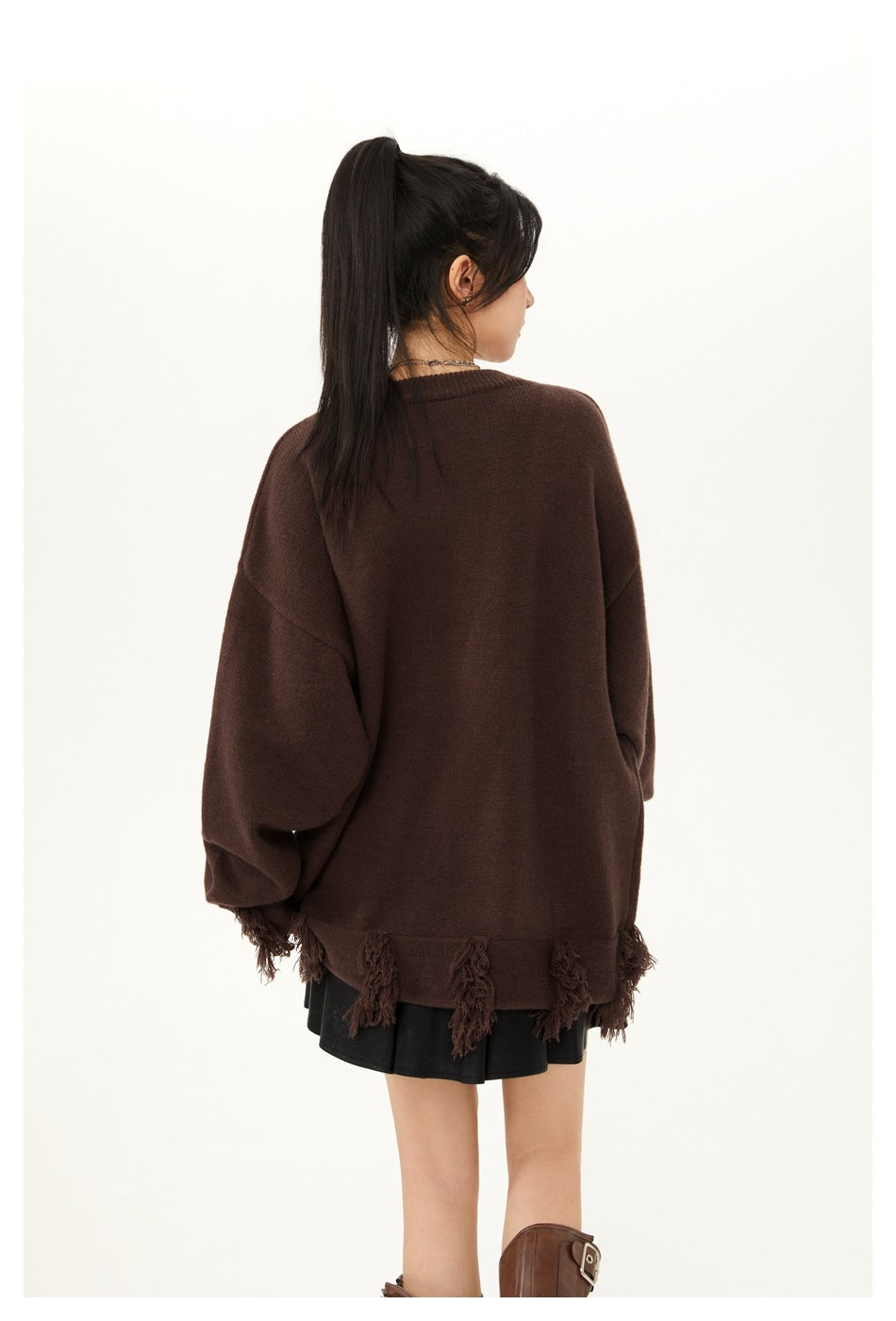 Back view of a model wearing a plain dark brown oversized sweater with tasseled hem and a black skirt.